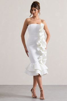 a woman is wearing a white dress with ruffles on the skirt and heels