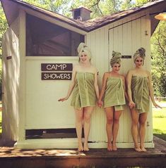 three women in green bathing suits standing next to a white shed with camp showerers written on it