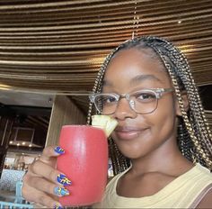 a woman holding a drink in her right hand and smiling at the camera while wearing glasses