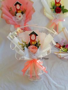 three small bouquets with flowers in them on a white tableclothed surface, one has an ornament and the other is a graduation cap