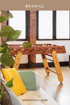 A brown outdoor football table with wooden legs and handles set in an indoor area in front of a brick wall with large windows