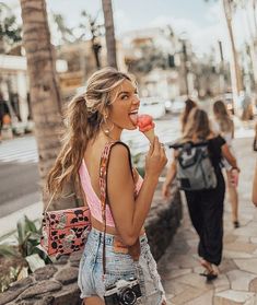 a woman eating a donut while walking down the street with other people behind her