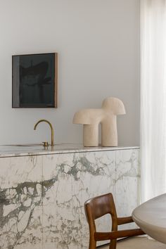 a kitchen with marble countertops and wooden chairs in front of a painting on the wall