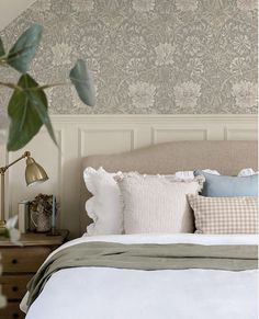 a bed with white sheets and pillows in front of a wallpapered headboard