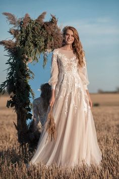 a woman in a wedding dress standing next to a tall grass arch with flowers on it