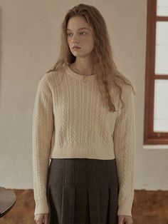 a woman standing in an empty room wearing a sweater and pleated skirt