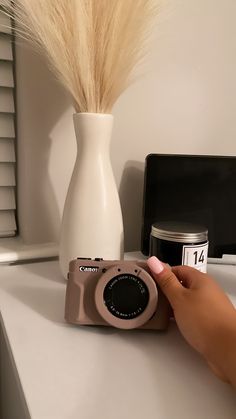 a person is taking a photo with a camera next to a vase on a table