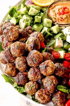 a white plate topped with meatballs and salad next to a bowl of dip sauce