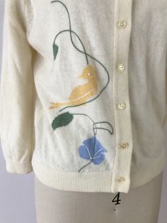 "7 DAY NO HASSLE RETURNS. This vintage cardigan circa 1950s to 1960s is knit in a soft wool and animal hair (probably mohair or angora) blend, with a bird and butterfly motif that is a mix of intarsia knit and embroidery. Full button up with a collar, 3/4 sleeves, and ribbed cuffs and hem. . M E A S U R E M E N T S . b u s t : 38\" w a i s t : 29\" s l e e v e . i n s e a m : 12.5\" g a r m e n t . l e n g t h : 21\" For more information on measurements, visit: http://www.foxburrowvintage.com/p/ Vintage Embroidered Cream Cardigan, Vintage Cream Embroidered Cardigan, Vintage Cream Sweater For Spring, Vintage Embroidered Sweater For Spring, Fitted Vintage Cardigan For Spring, Retro Cream Sweater For Spring, Vintage Spring Cardigan With Button Closure, Retro Embroidered Cardigan For Winter, Retro Embroidered Winter Cardigan