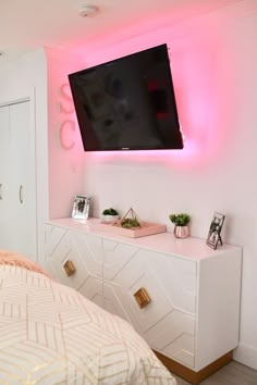 a flat screen tv mounted to the side of a wall above a white dresser in a bedroom