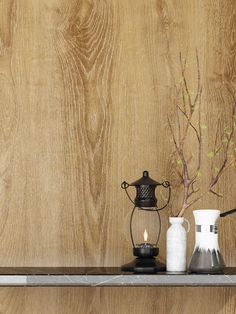 two vases and a candle on a shelf in front of a wood paneled wall