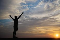 a man standing on top of a field with his arms in the air at sunset