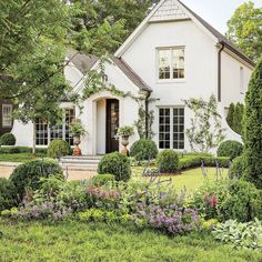 a white house with lots of bushes and flowers around it's front door, surrounded by greenery