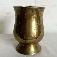 an antique brass cup with designs on the side sitting on a white tableclothed surface