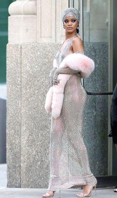 a woman in a silver dress and fur stoler is walking down the street with her hand on her hip