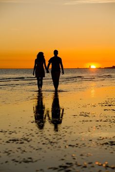 two people walking on the beach at sunset with their hands in each others'pockets