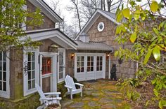 two white lawn chairs sitting in front of a stone building with windows and doors on each side