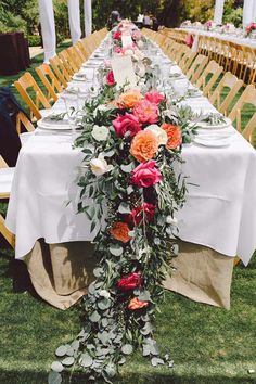 a long table with flowers and greenery is set up for an outdoor wedding reception