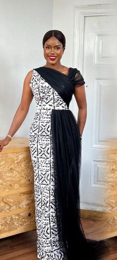 This Ankara Gown with Draped Black Tulle is crafted from premium Ankara fabric, showcasing a bold monochrome pattern that's both timeless and chic. The one-shoulder design adds a contemporary twist, highlighting your neckline and shoulders, while the asymmetrical cut ensures a flattering silhouette for every body type. The standout feature of this gown is the draped black tulle overlay, adding a layer of intrigue and glamour. The tulle cascades effortlessly from the shoulder, creating a dramatic effect that's perfect for making an entrance at any special occasion. Whether you're attending a wedding, gala, or any formal event, this gown is designed to turn heads and leave a lasting impression. With its exquisite design and impeccable craftsmanship, this gown is not just a piece of clothing African Wedding Guest Dress, Gala Night Dress, Print Formal Dress, Long Pencil Dress, Dress Gala, Gala Night, Dress African Print, Ankara Dress Designs, Long African Dresses