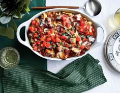 a casserole dish with tomatoes and other toppings on a green table cloth