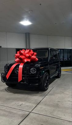 a black jeep with a red bow on it's hood parked in a parking garage