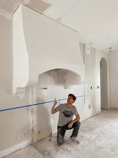 a man kneeling on the floor in front of a white wall with blue tape around it