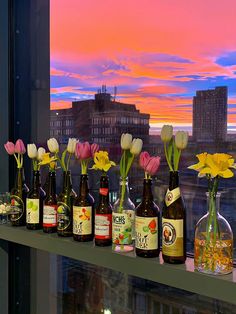 several bottles and vases filled with flowers on a window sill in front of a cityscape