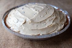 a pie with white frosting sitting on top of a cloth covered table next to a cupcake tin