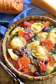 a bowl filled with pasta and vegetables on top of a wooden table next to bread