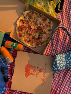 an open pizza box sitting on top of a picnic blanket next to other food items