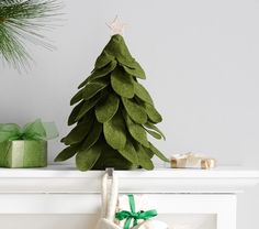 a green christmas tree sitting on top of a mantle next to presents and a bag