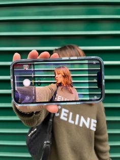 a woman taking a selfie with her cell phone in front of a green wall