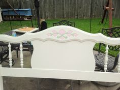 a white bed frame with pink flowers on the headboard and foot board, sitting outside