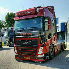 a red volvo semi truck parked in front of a building with other trucks behind it