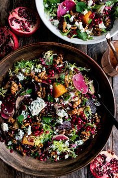 two bowls filled with salad on top of a wooden table next to sliced pomegranates