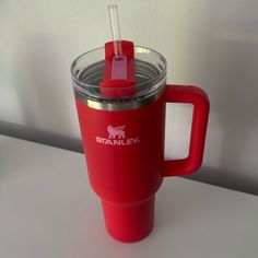 a red travel mug with a straw in the lid and handle is sitting on a table