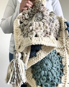 a woman holding a crocheted blanket with tassels