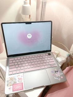 an open laptop computer sitting on top of a white desk next to a pink pillow