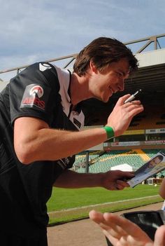 a young man signing autographs for fans at a sporting event in front of an empty stadium