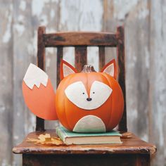 an orange pumpkin with a fox face sitting on top of a wooden chair next to leaves