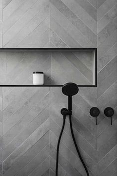 a bathroom with grey tile and black shower faucet next to it's wall