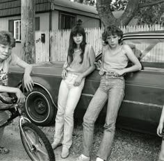 three young women sitting on the back of a car next to a bike and bicycle