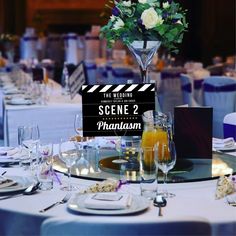 a table set up for an event with flowers in a tall glass vase on top