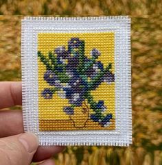 a hand holding up a small cross stitched card with flowers on it's side