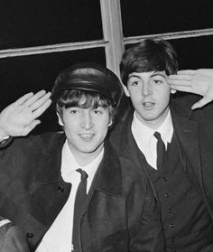 two young men sitting next to each other in suits and ties, one wearing a hat