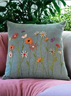 an embroidered pillow with daisies and other flowers on it sitting on a pink couch