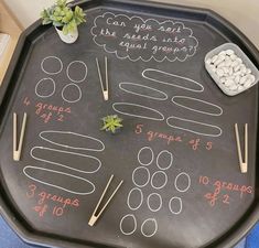 a black tray with writing on it that has plants and sticks in the shape of numbers