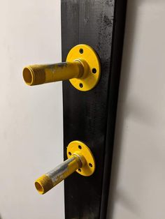 two yellow pipe holders are attached to a black and white wall with screws on it