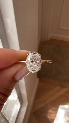 a woman's hand holding an engagement ring in front of a window with sunlight streaming through it