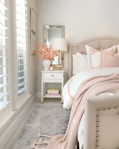 a white bed with pink pillows and blankets on top of it next to a window